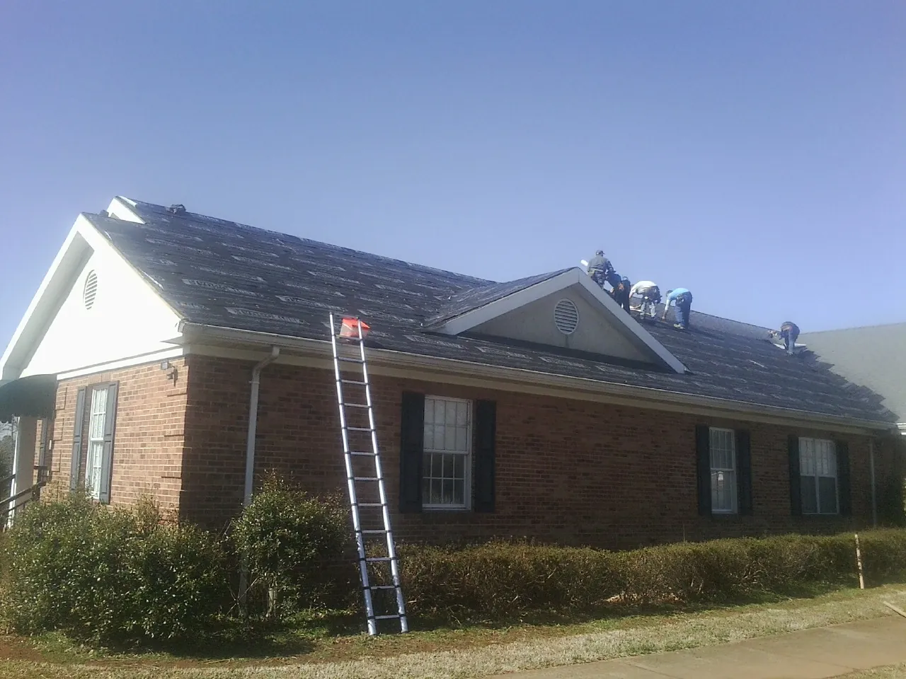 Crew tearing shingles off a brick ranch roof with a ladder set — Emergency Roof Repair work by our crew in Valley Park