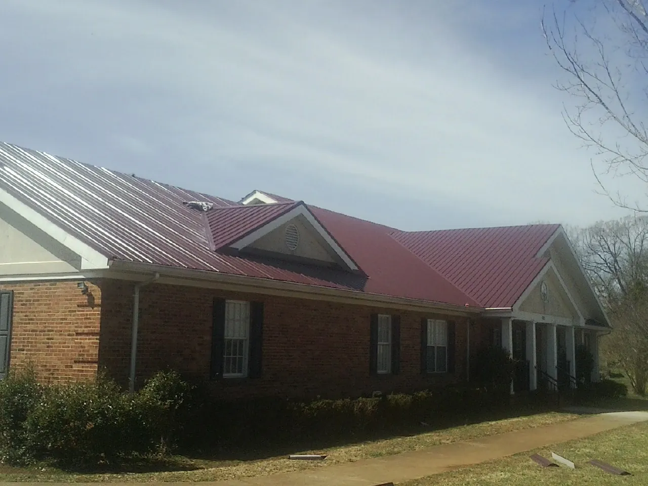 Red metal roof with gabled entries on a long brick building, from a Hail Damage Roof Repair job in Valley Park