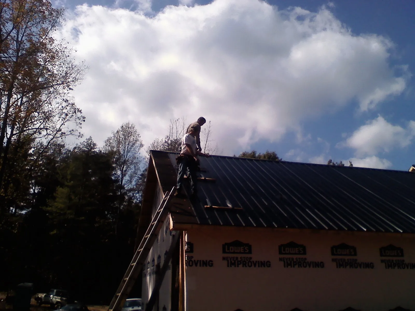 Roofer fastening dark metal panels high against a cloudy sky, from a Roof Inspection job in Valley Park